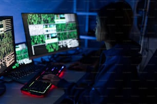 A young woman hacker by computer in the dark room at night, cyberwar concept.