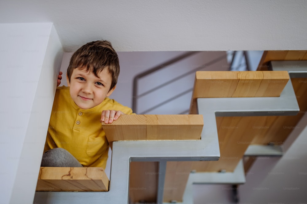 Un niño pequeño escondido en una escalera de madera y mirando hacia abajo en casa