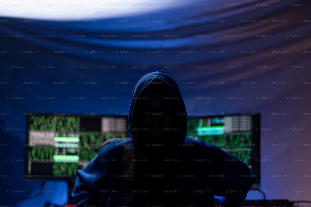 Un hacker anónimo encapuchado por computadora en la habitación oscura por la noche, concepto de guerra cibernética.