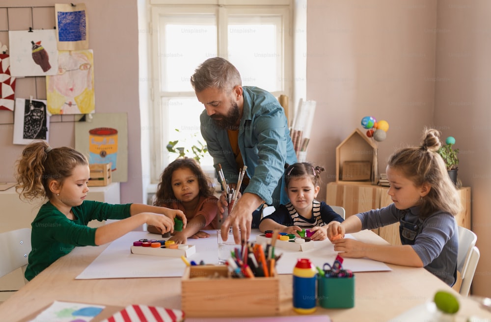 Eine Gruppe kleiner Kinder, die während des kreativen Kunst- und Handwerksunterrichts drinnen in der Schule an einem Projekt mit dem Lehrer arbeiten.