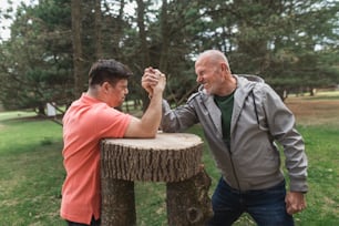 A happy senior father with his adult son with Down syndrome arm wrestling in park.