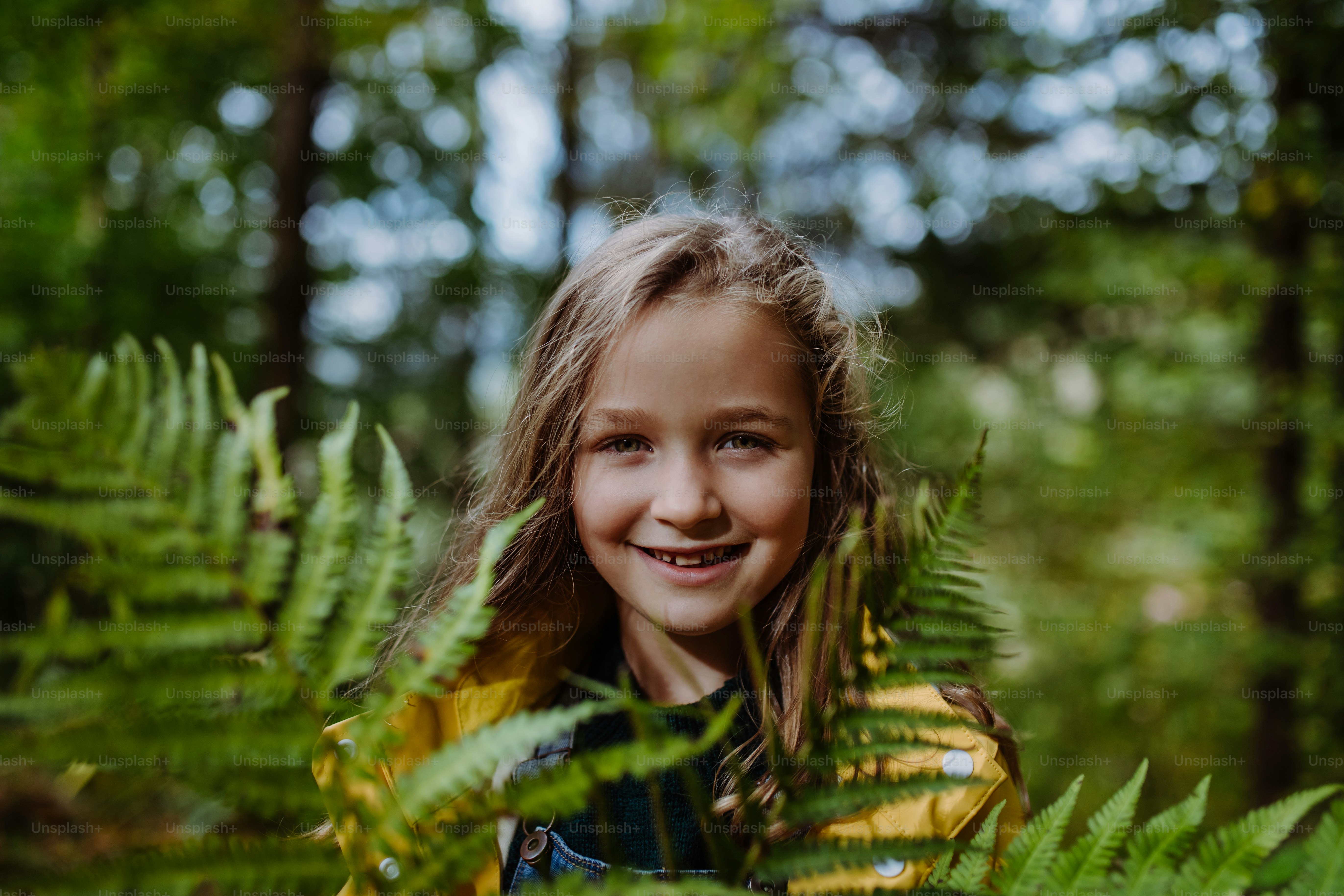 A happy little girl holding fern and looking at camera outdoors in ...