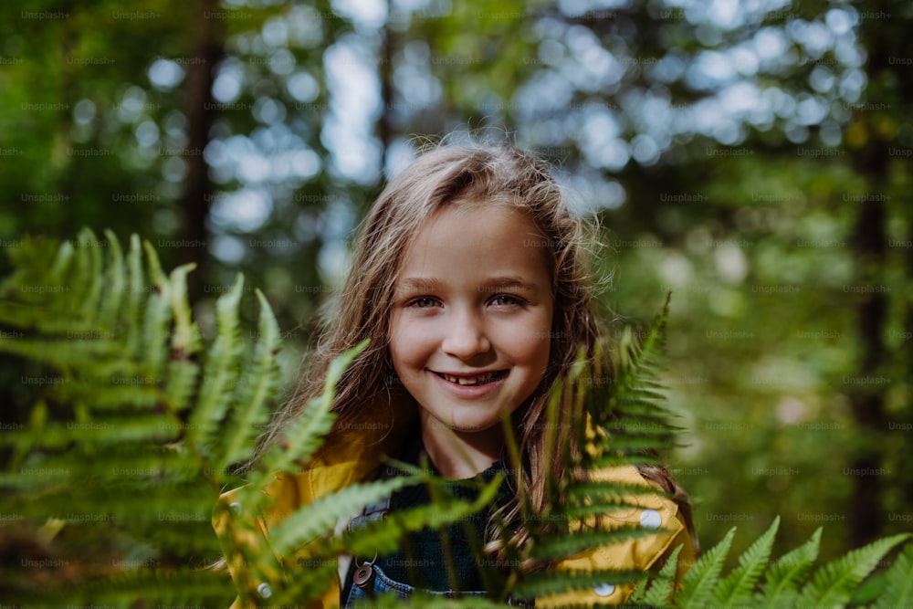 Une petite fille heureuse tenant une fougère et regardant la caméra à l’extérieur dans la forêt.