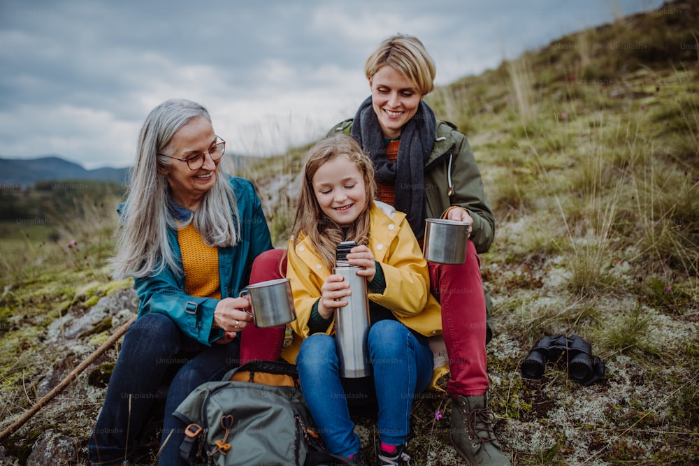 Una bambina con la madre e la nonna sedute e bevendo tè caldo in cima alla montagna.
