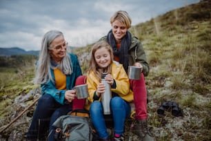 A small girl with mother and grandmother sitting and drinking hot tea on top of mountain.