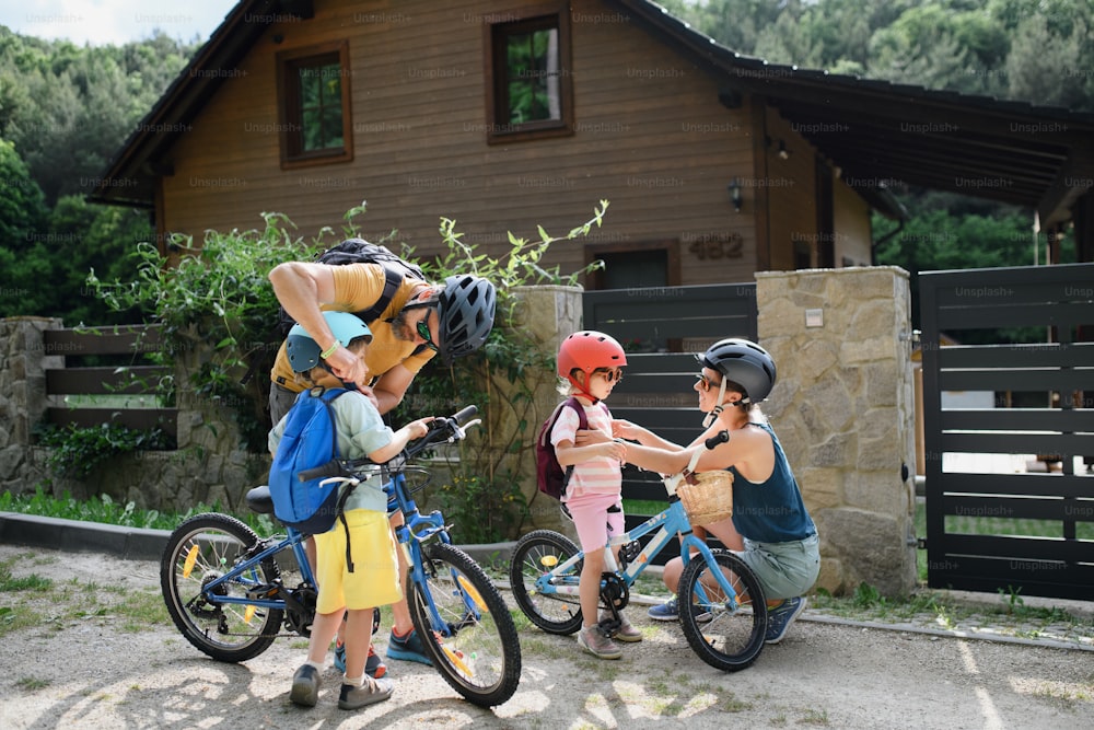 Un portrait d’une jeune famille avec de petits enfants se préparant à faire du vélo, debout avec des vélos devant la maison.