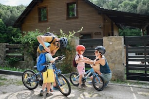 Un ritratto di giovane famiglia con bambini piccoli che si prepara per un giro in bicicletta, in piedi con le biciclette davanti alla casa.