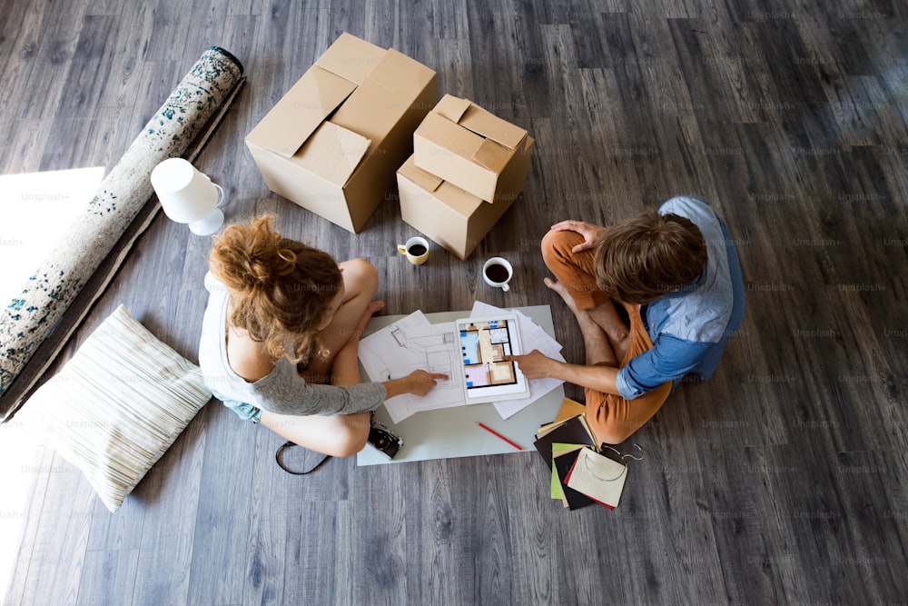Young married couple moving in new house, sitting on the floor near cardboard boxes, planning.