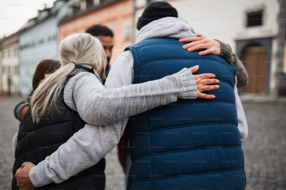 A rear view of community service volunteers hugging together outdoors in street