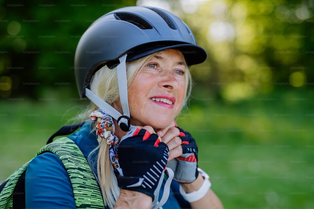 Un couple de personnes âgées actives faisant du vélo au parc d’été, une femme met un casque, un concept de mode de vie sain.