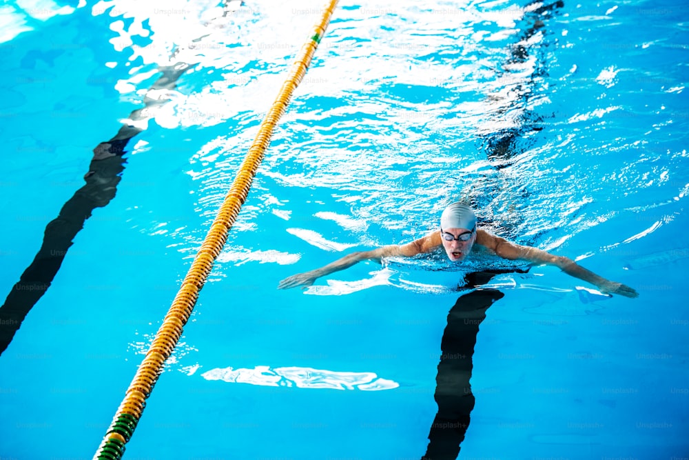 Senior Mann schwimmt in einem Hallenbad. Aktiver Rentner mit Spaß am Sport.