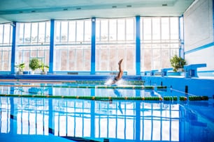 Senior man in an indoor swimming pool. Active pensioner enjoying sport. An old man jumping in the pool.