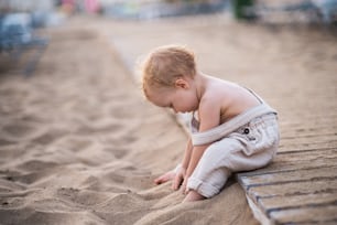A cute small toddler girl sitting on beach on summer holiday, playing. Copy space.