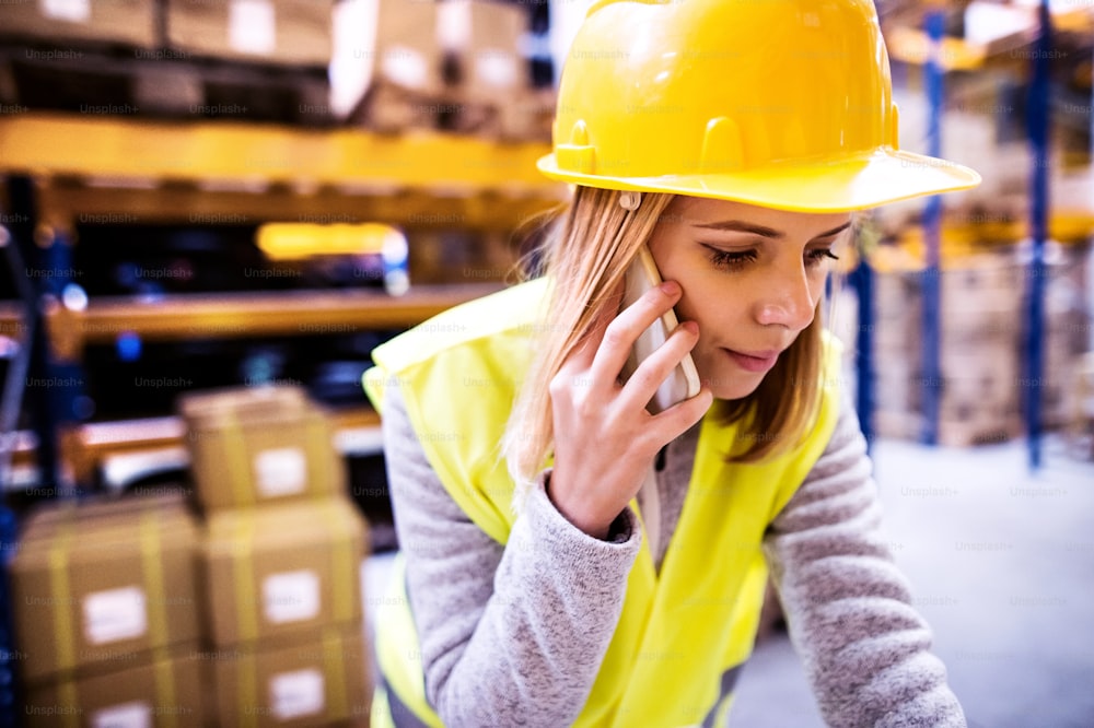 Young female warehouse worker with smartphone. A supervisor making a phone call.