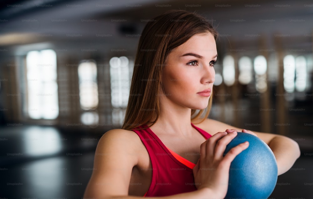 A portrait of a beautiful young girl or woman doing exercise with a ball in a gym.