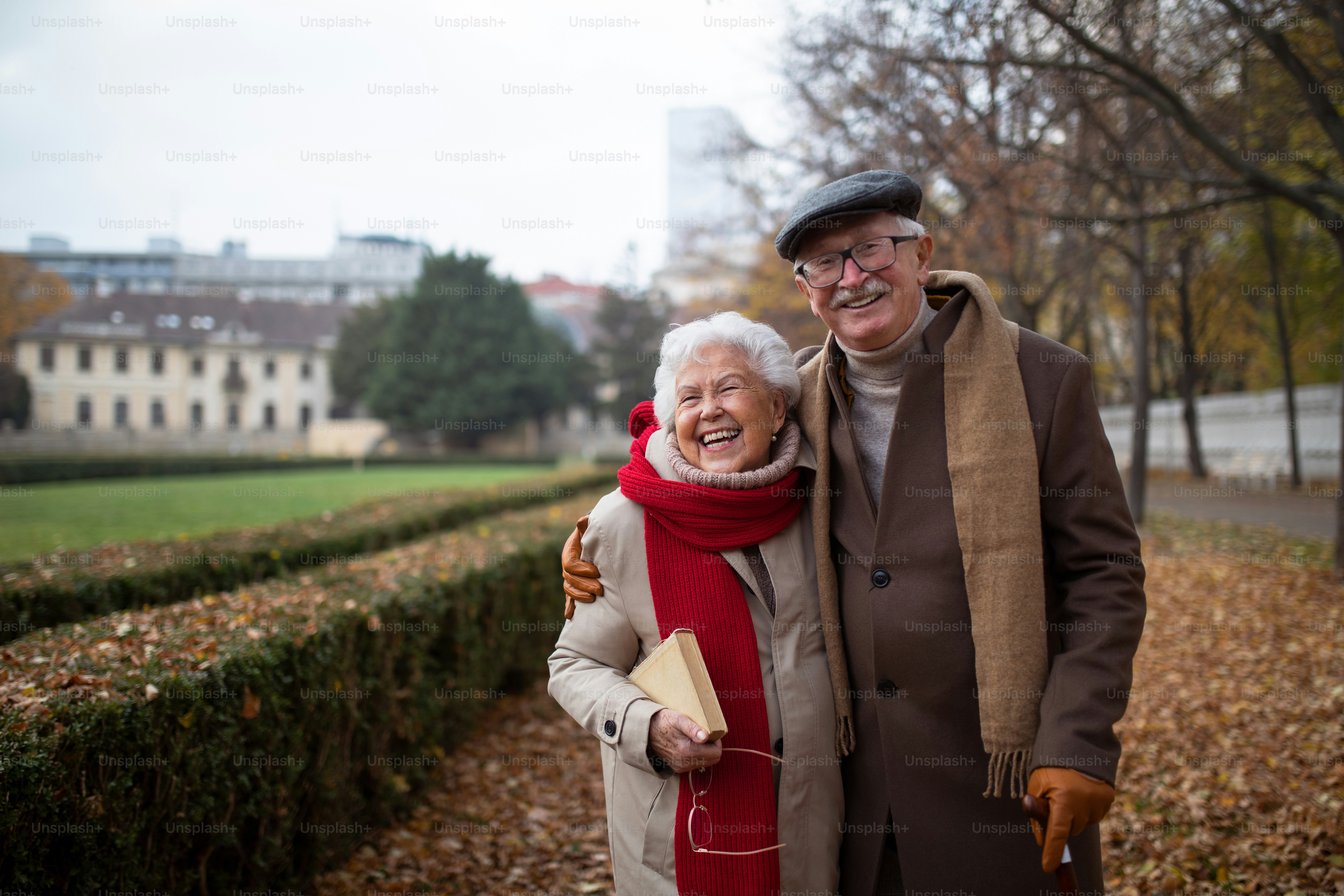 Una feliz pareja de ancianos en un paseo al aire libre en el parque en otoño, abrazándose, riendo y mirando a la cámara