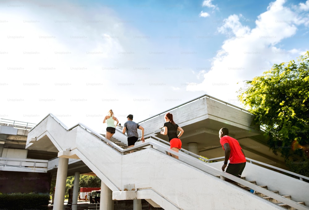 Jovens bonitos na cidade correndo juntos pelas escadas, vista traseira.