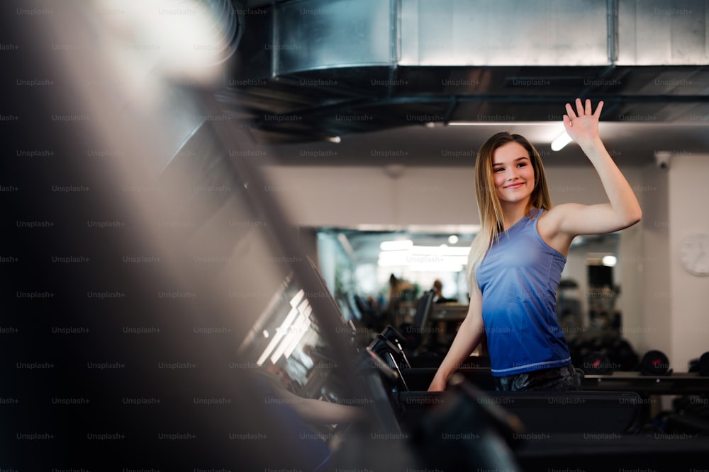 Un retrato de una hermosa joven o mujer saludando a alguien cuando hace ejercicio cardiovascular en un gimnasio.