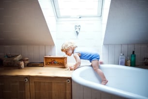 浴槽から這い上がる小さな幼児の男の子。家庭内事故。バスルームでの危険な状況。