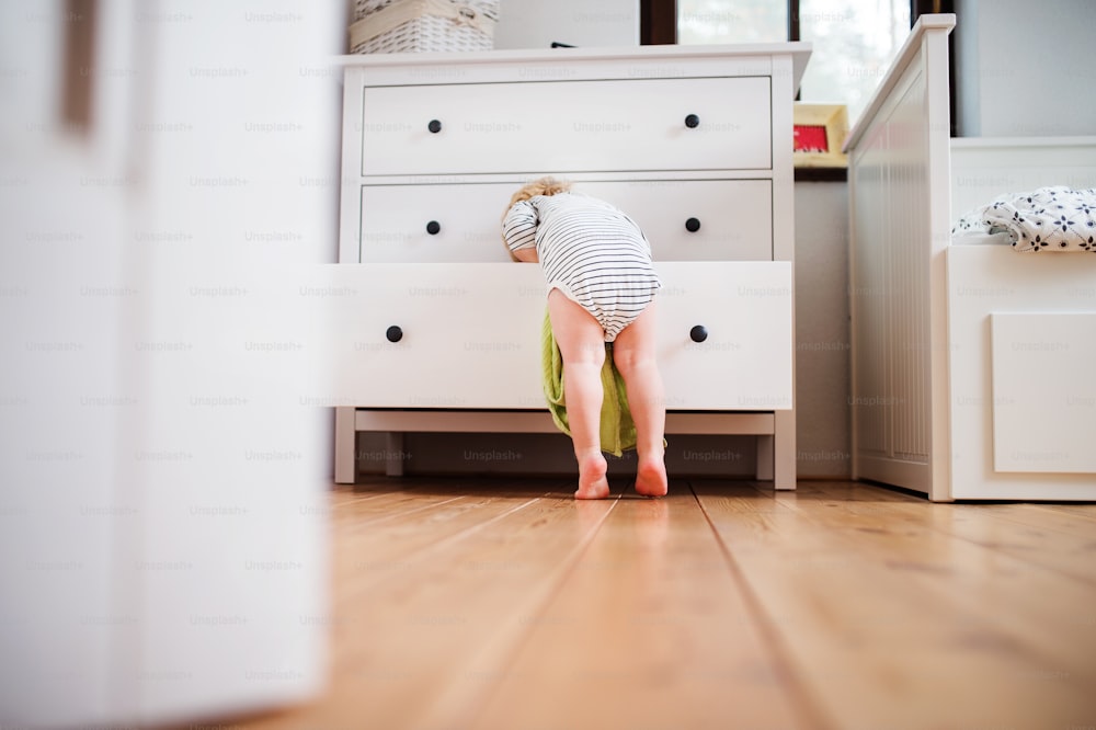 Little toddler boy opening a drawer. Domestic accident. Dangerous situation at home. Rear view.