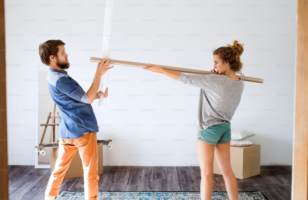 Young married couple moving in new house, fighting with rolls of wrapping paper