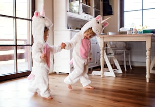 Two toddler children with white unicorn masks playing indoors at home.