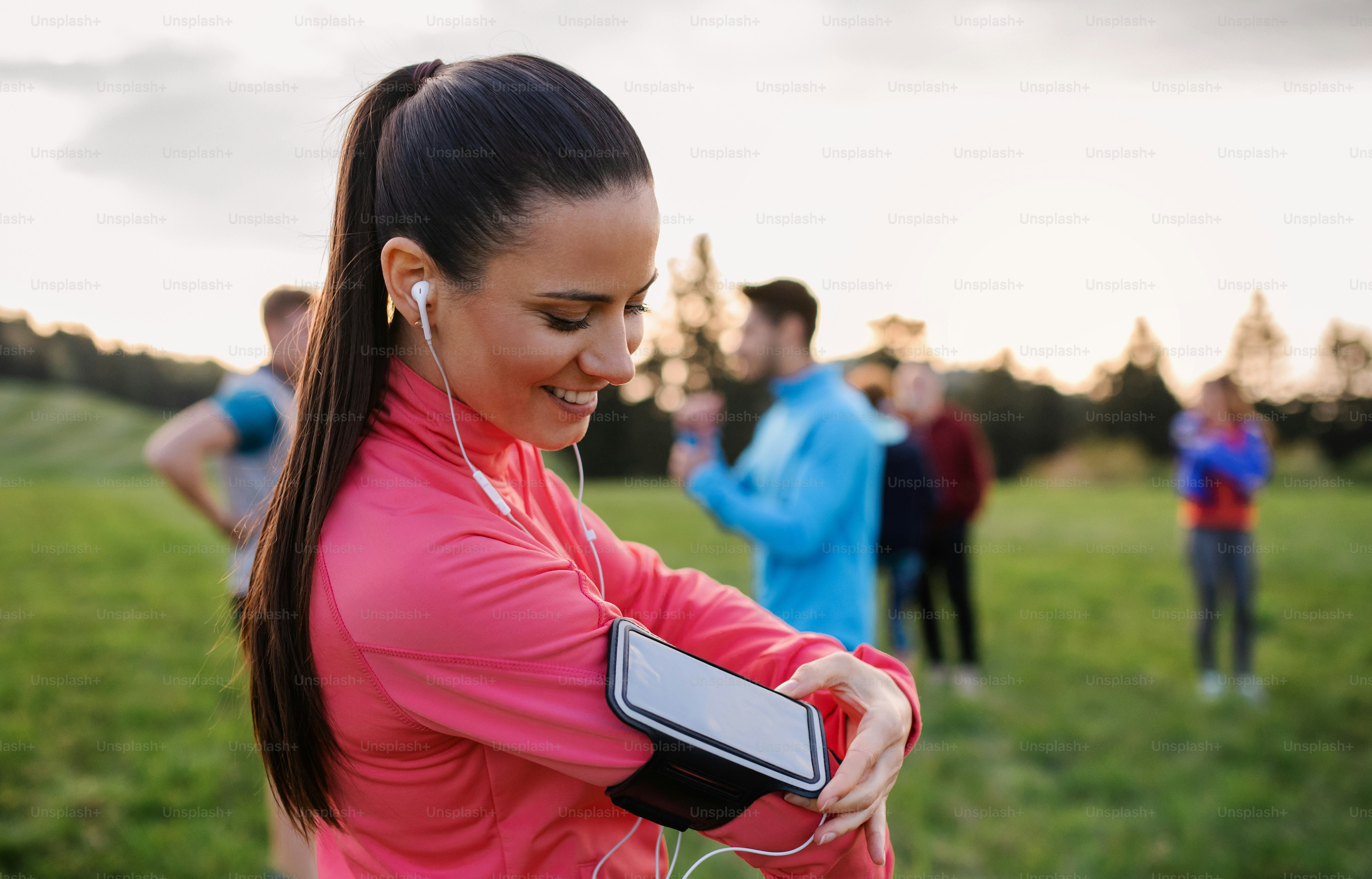 A portrait of young woman with earphones and group of people doing exercise in nature, resting