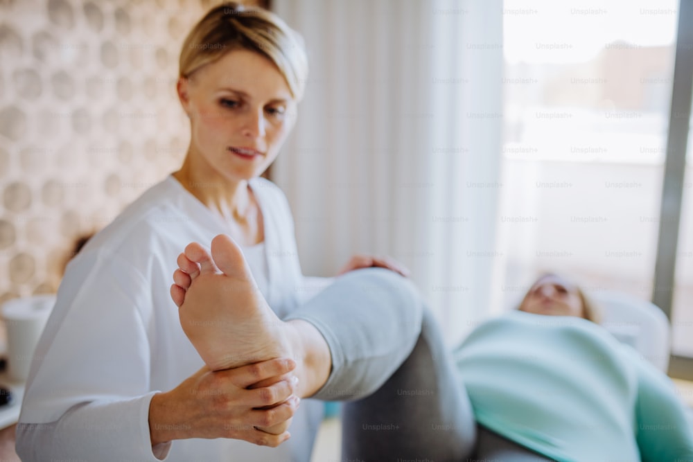 Une femme kinésithérapeute adulte moyenne faisant de l’exercice avec une femme en surpoids à l’intérieur dans un centre de rééducation