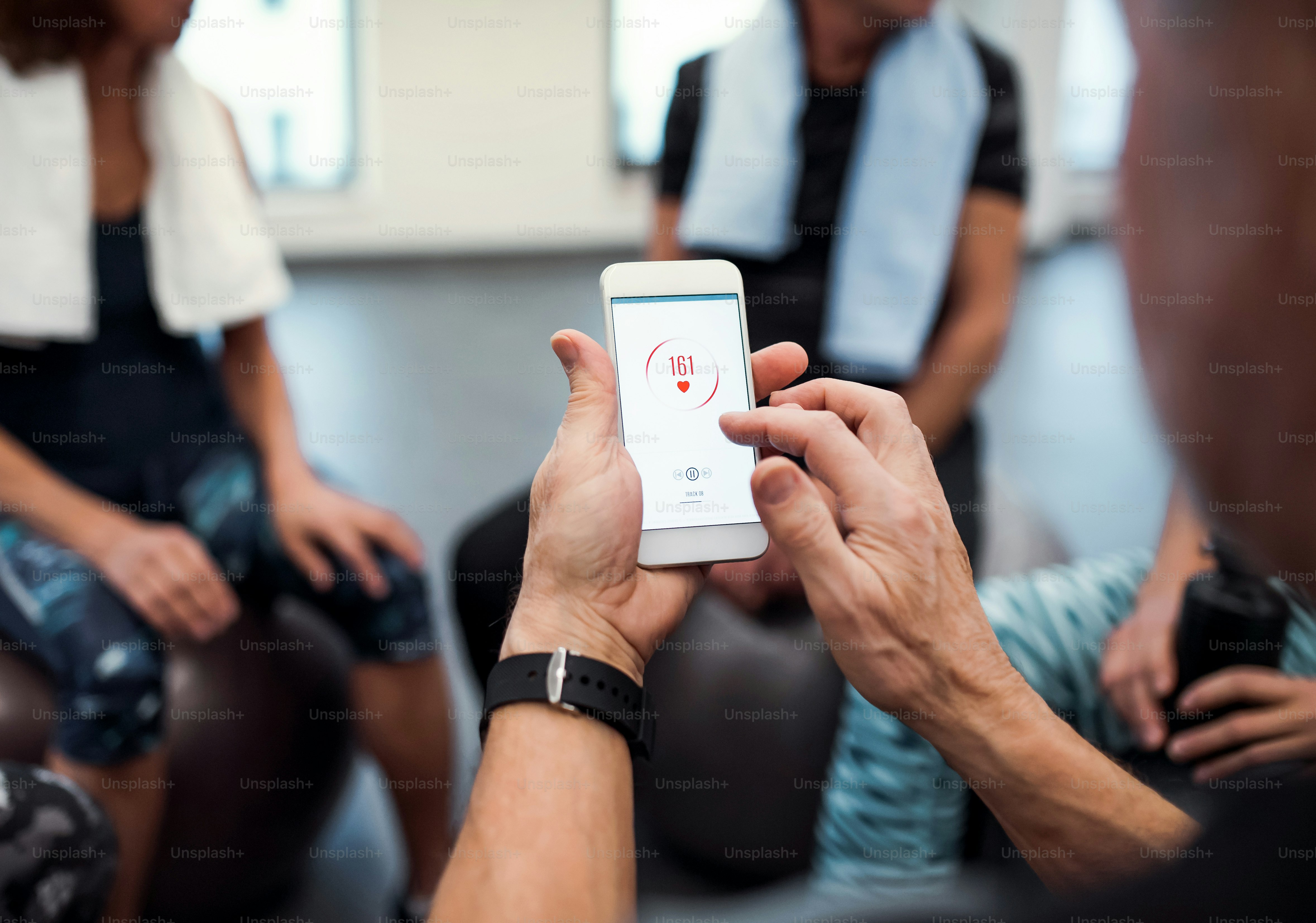 ジムでスマートフォンを手に、運動後に心拍数をチェックし、安静にしている高齢者のグループの真ん中。
