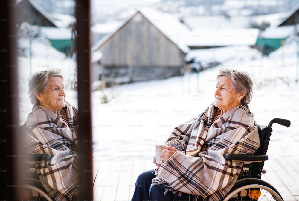 A happy senior woman outside on a terrace in winter, holding a cup of coffee.