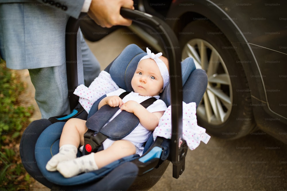 Homme méconnaissable portant sa petite fille dans un siège d’auto., entrant dans la voiture.