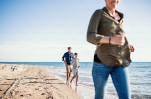 Familia joven con hijo pequeño corriendo al aire libre en la playa, una sección media.