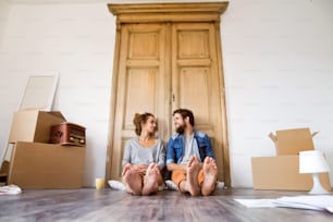 Young married couple moving in new house, lying on the floor near cardboard boxes, resting.