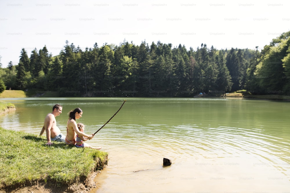 Madre y padre jóvenes con su hija en el lago. Calor y agua en verano.