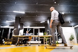 Two young businesspeople in the office at night working late. Hipster businessman on longboard.