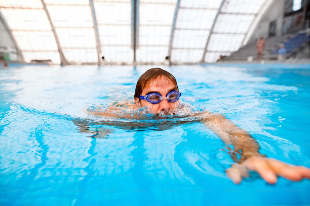 Uomo che nuota in una piscina coperta. Nuotatore professionista che si allena in piscina.