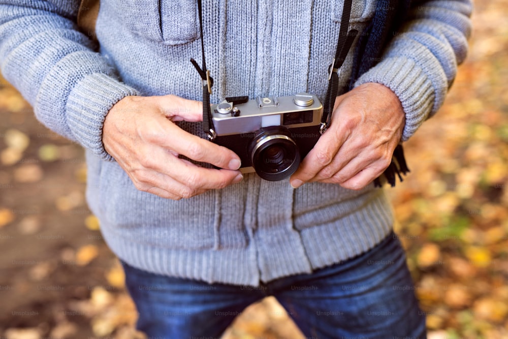 Unrecognizable senior man on a walk in a beautiful autumn nature. A man holding camera. Close up.