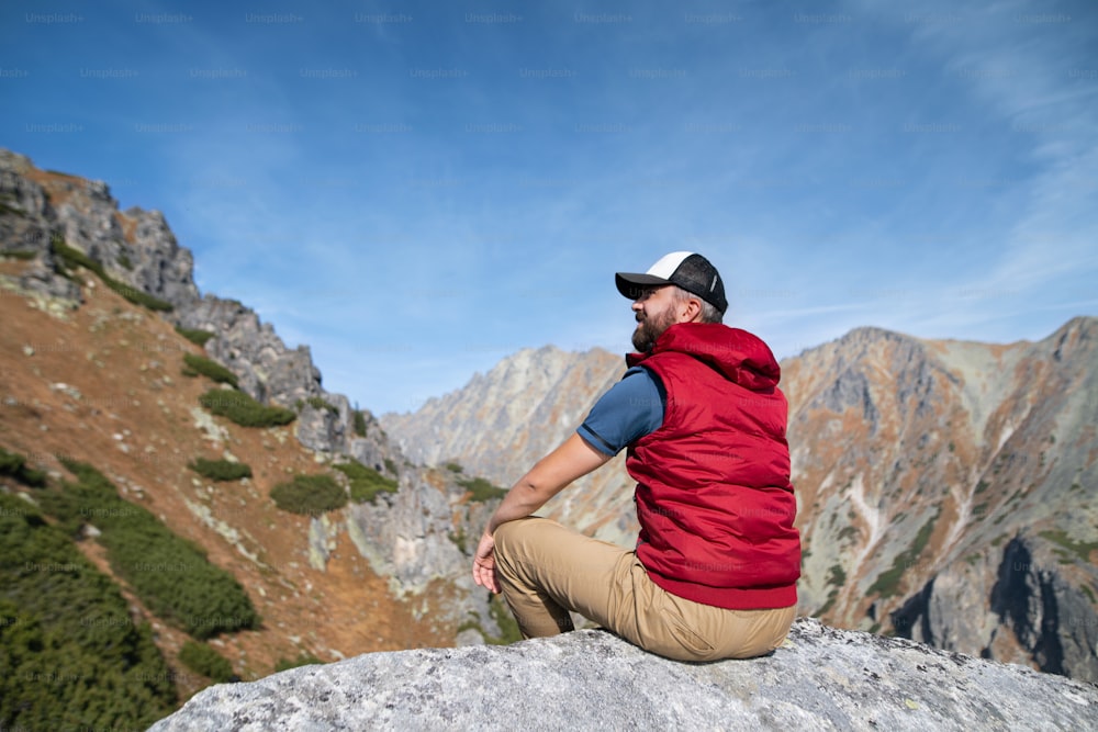 Rear view of mature man hiking in mountains in autumn, resting. Copy space.