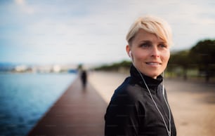 A portrait of young sportswoman with earphones standing outdoors on beach. Copy space.