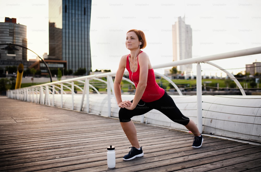 A young woman doing exercise on bridge outdoors in city, stretching.