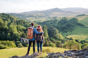 バックパックを背負った若い観光客のカップルが自然の中をハイキングし、休んでいる後ろ姿。