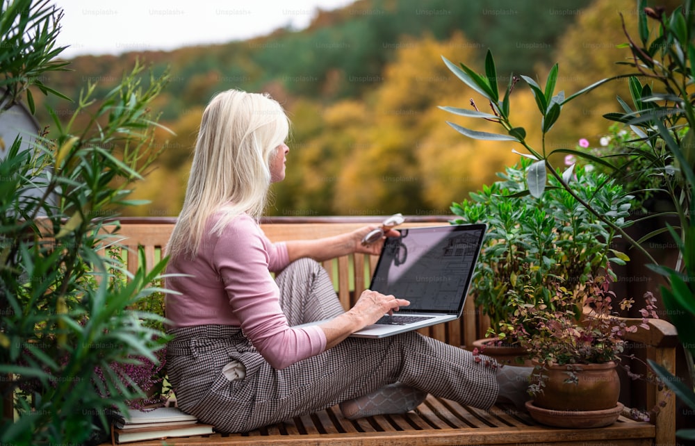 Une femme architecte chevronnée avec un ordinateur portable, assise à l’extérieur sur la terrasse, en train de travailler.