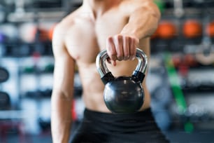 Unrecognizable young fit man in modern gym doing kettlebell swings. Close up.