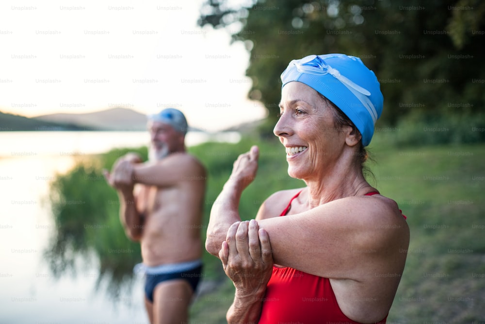 Senior couple in swimsuit standing in lake outdoors before swimming, doing exercise.