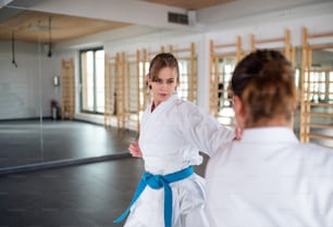 Zwei junge Frauen üben Karate drinnen im Fitnessstudio.