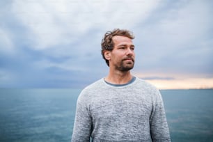 Portrait of mature man standing outdoors on beach at dusk.