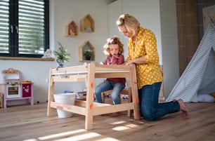 A cute small girl with mother in bedroom indoors at home, drawing pictures.