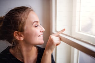 A close-up of young happy female student sitting on window sill.
