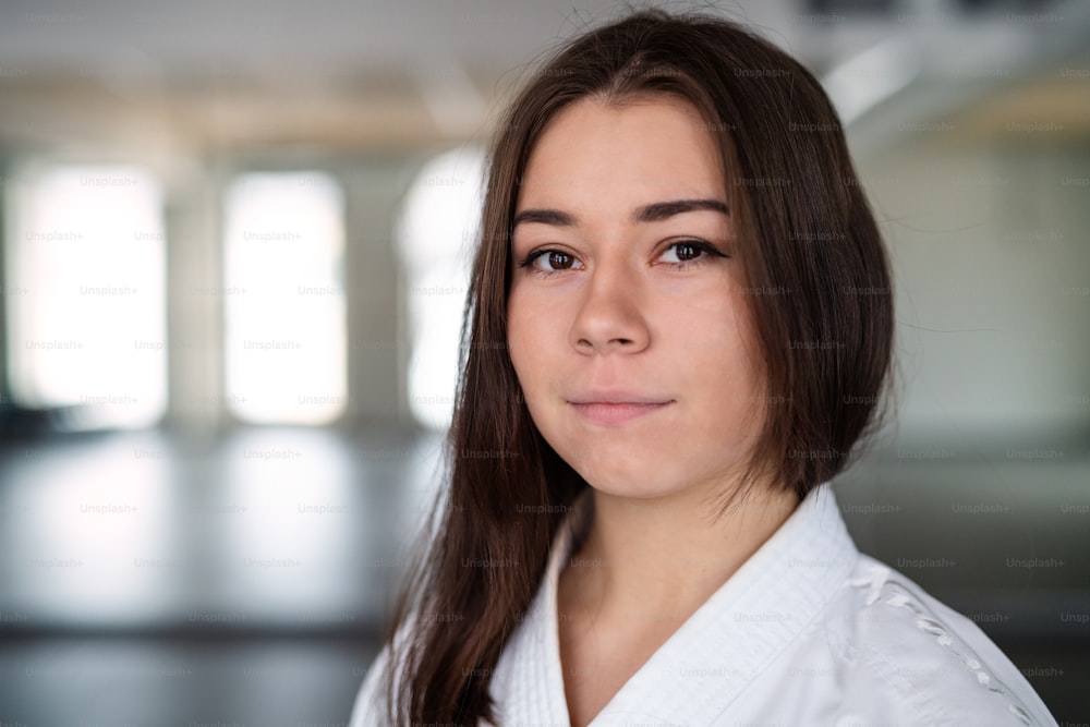 Ein Porträt einer jungen Karatefrau, die drinnen im Fitnessstudio steht und in die Kamera schaut.