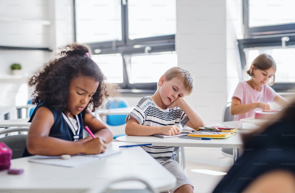 A small tired and bored school boy sitting at the desk in classroom, sleeping.